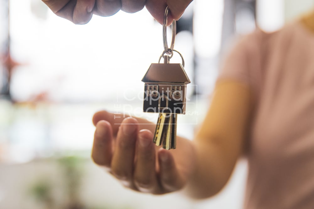Hands passing keys with a small house-shaped keychain.
