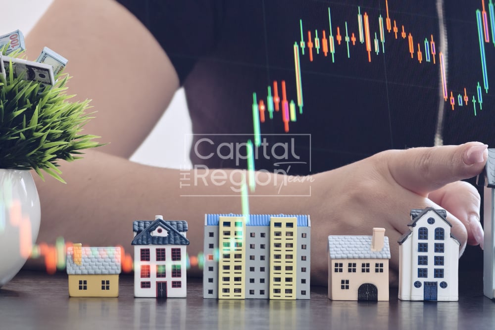 Miniature houses beneath a financial chart, with a hand reaching toward them.