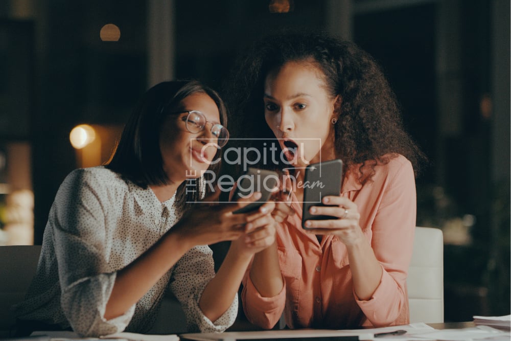 Two women review a tablet together at a table in a warmly lit interior.