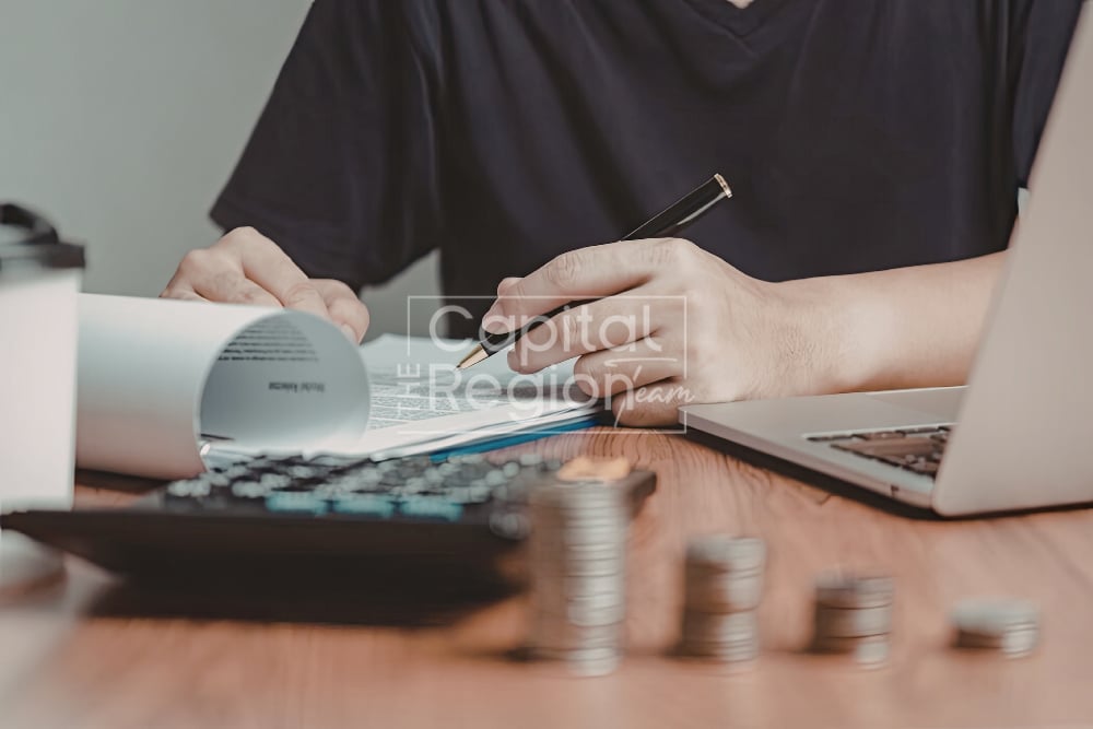 Person reviewing paperwork beside a calculator, laptop, and stacks of coins.