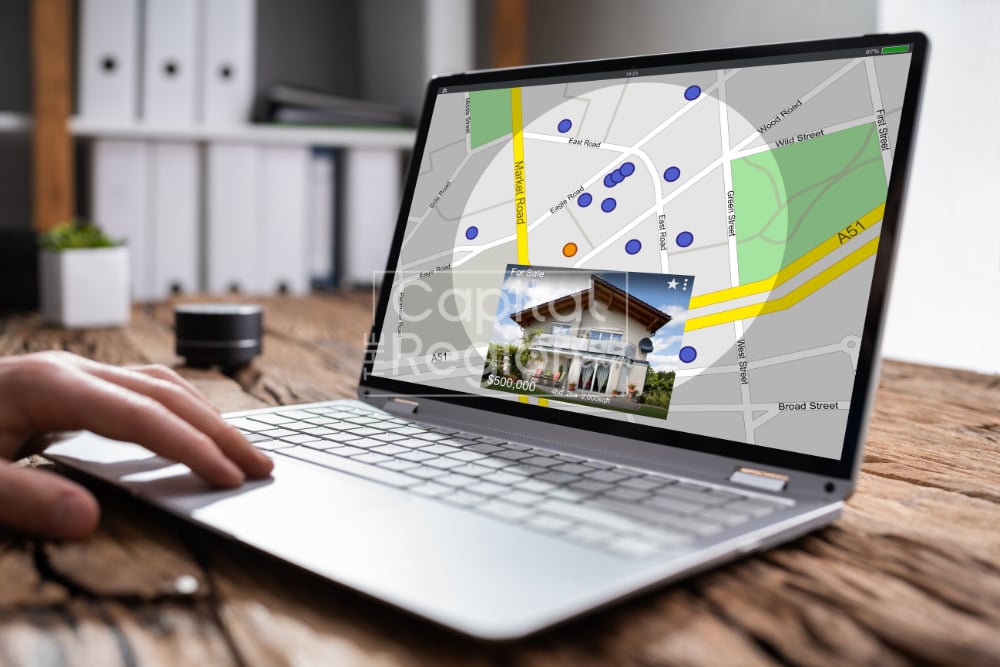 Hand using a laptop to browse a real estate map with home listings.