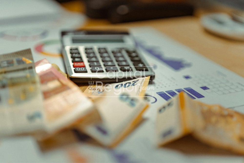 Calculator on financial paperwork and charts, with banknotes and coins scattered across the desk.