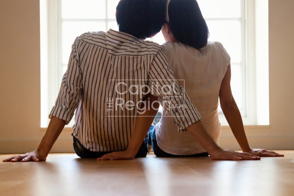 A couple sits together on the floor in front of a sunlit window.