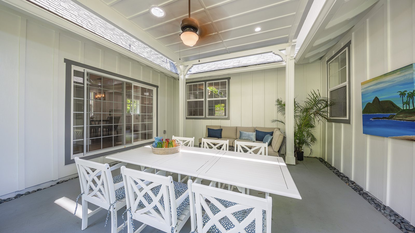 Covered lanai with a white dining table and chairs beside a single-family home