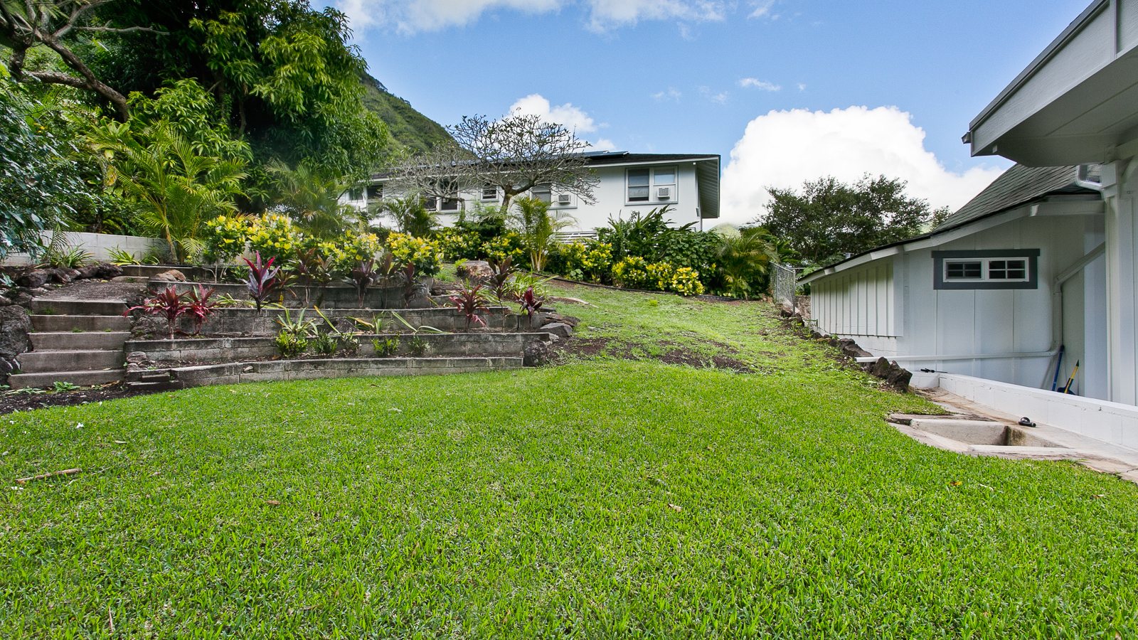 Sloped lawn and retaining wall behind a Honolulu valley home with green hills beyond
