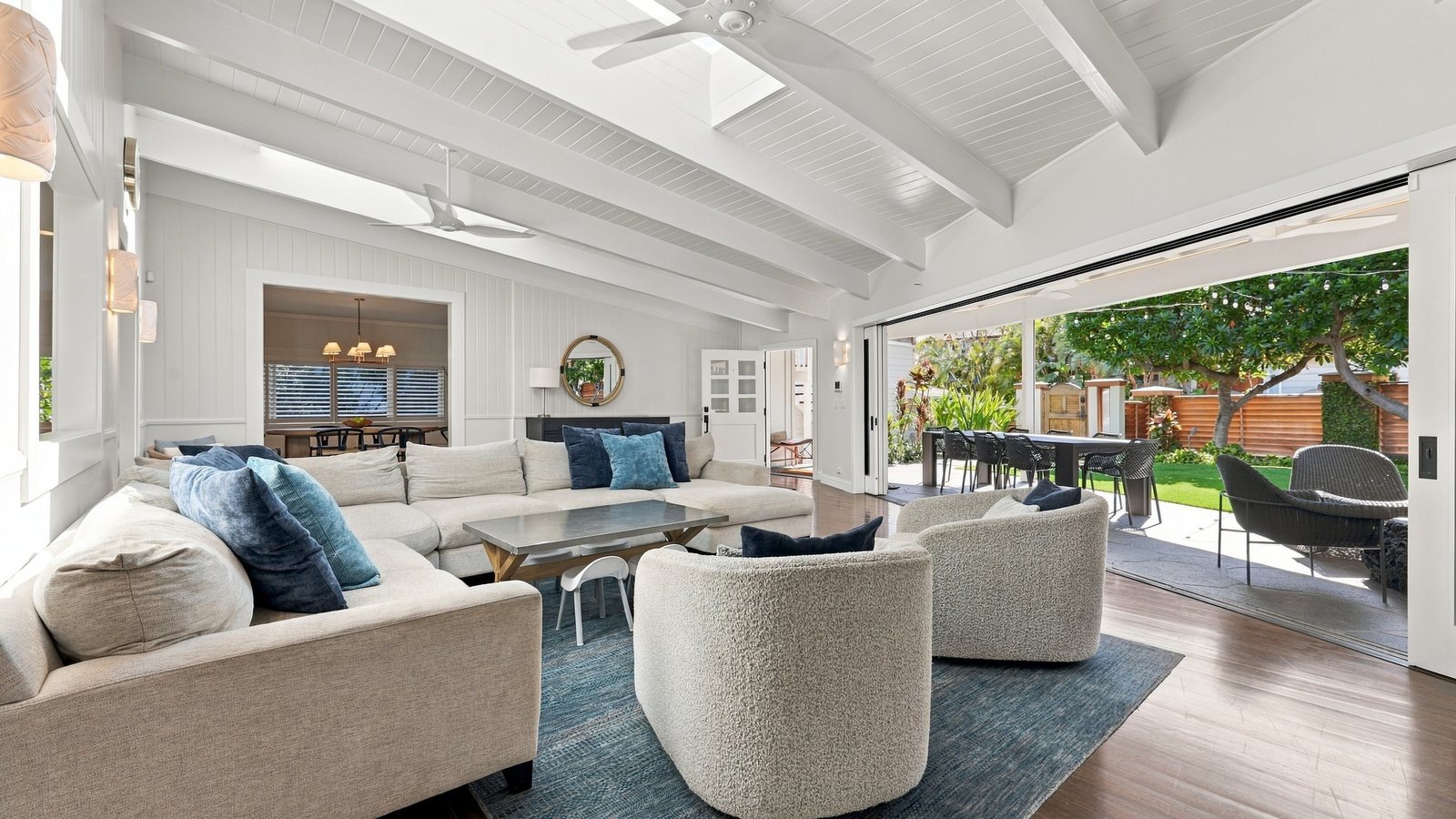 Bright staged living room with white walls, wood floors and open sliding doors to a garden lanai