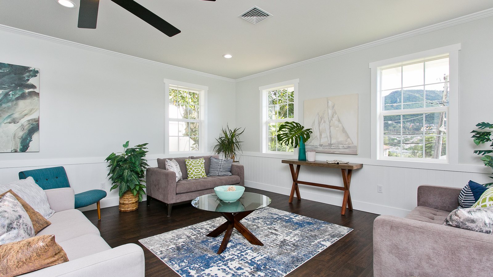 Bright living room with dark wood floors, white sofas and ceiling fan in a Manoa home