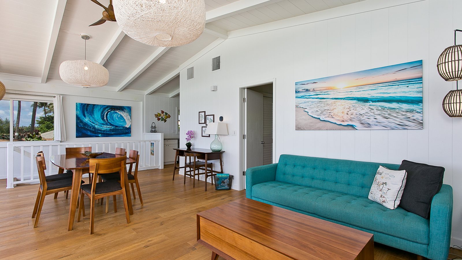 Open living and dining room with a teal sofa, wood floors and ocean art in a North Shore home
