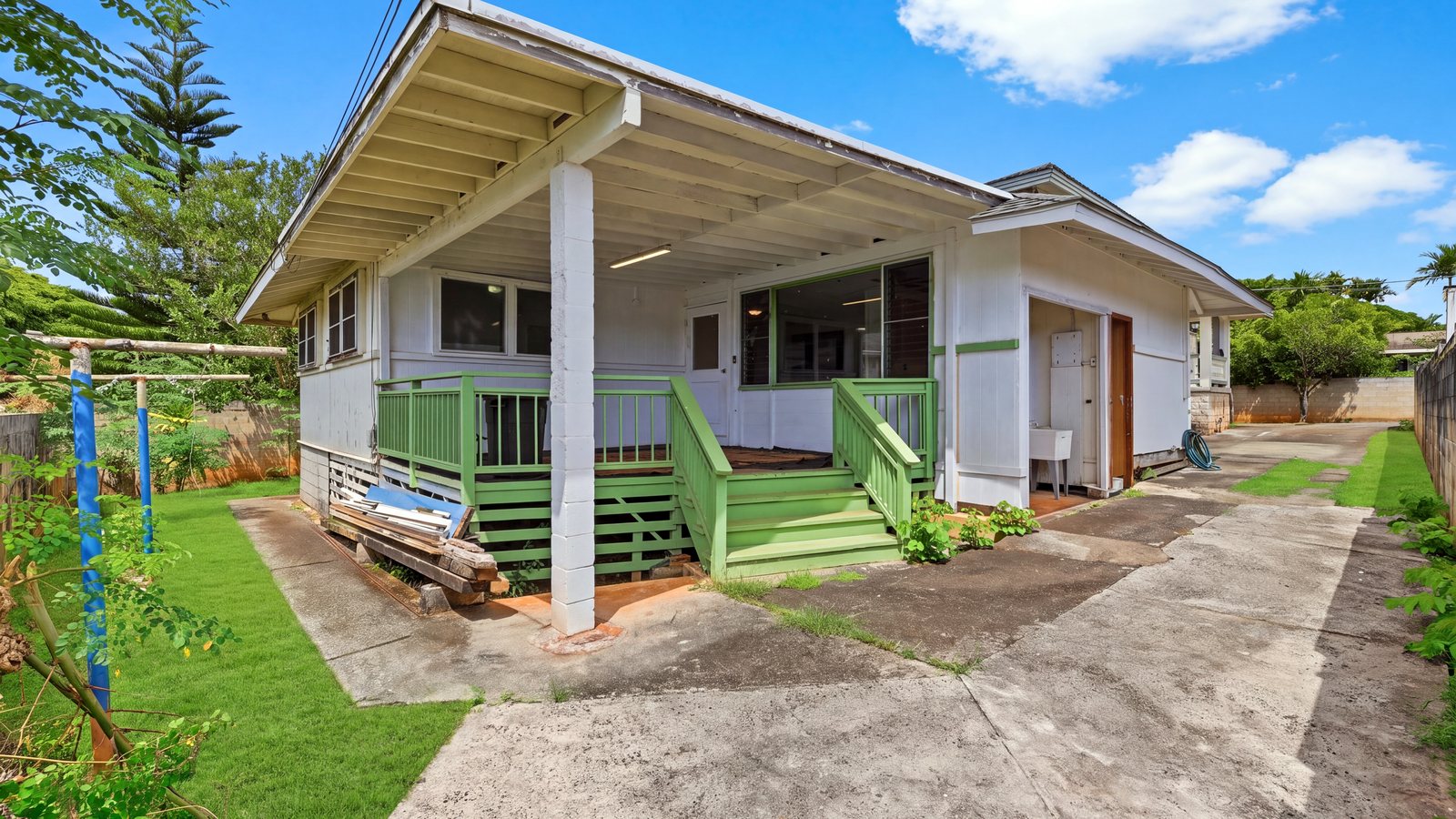 Older single-wall Honolulu home with a covered lanai, green railings and a concrete driveway