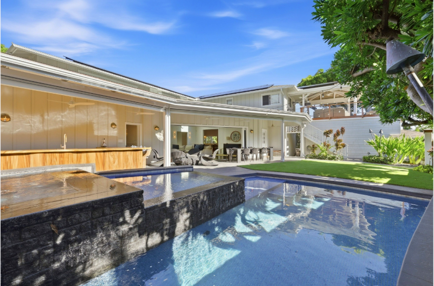 The pool, spa, and outdoor kitchen at 245 Palaoa Place, framed by lush landscaping
