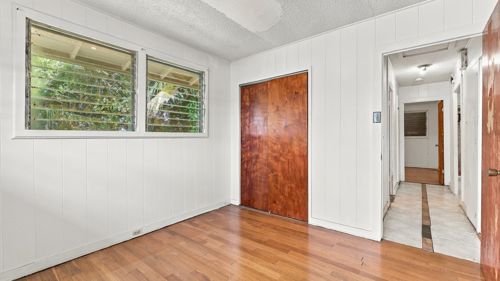 Empty bedroom with wood floors, white walls and louvered windows between tenants