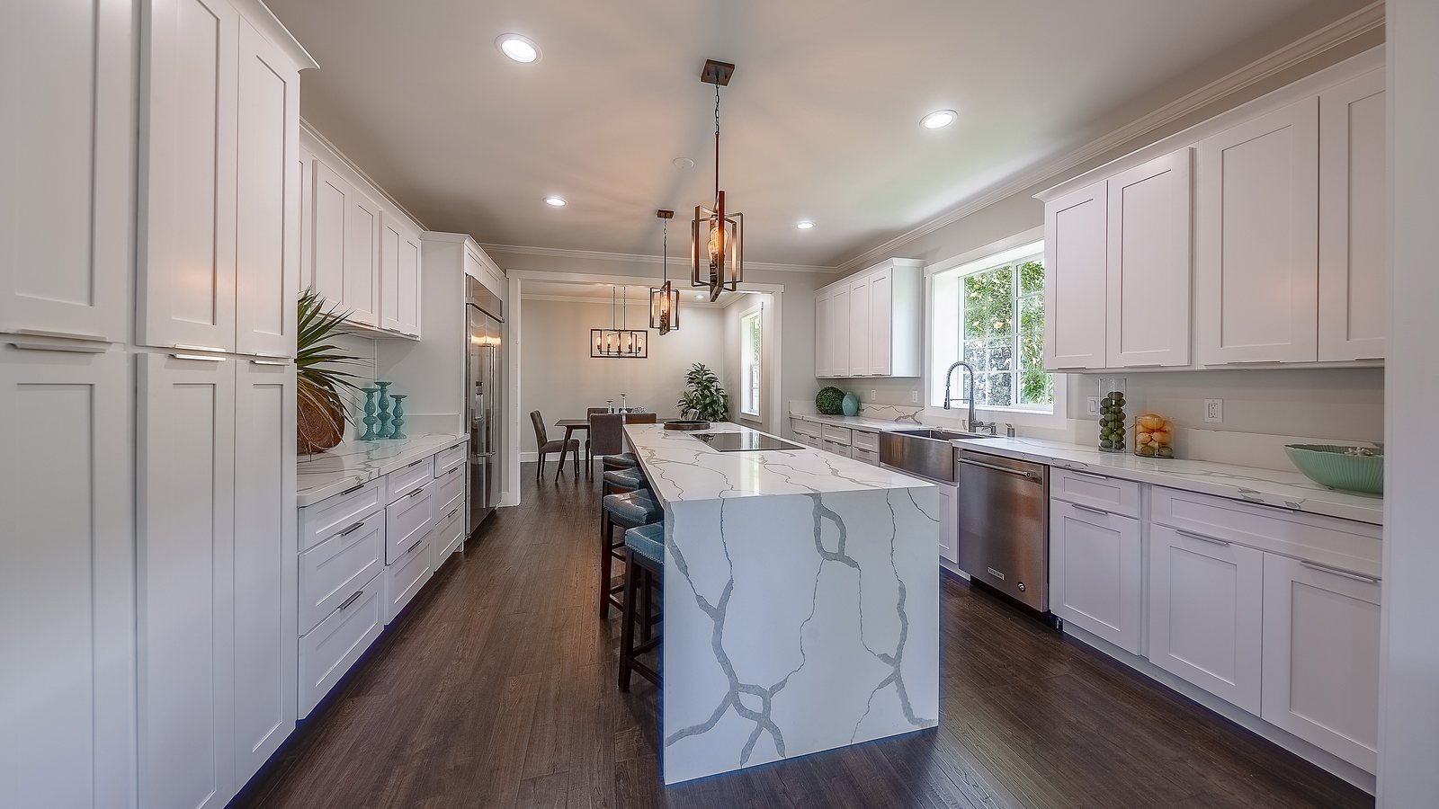 White kitchen with a long marble island and pendant lights