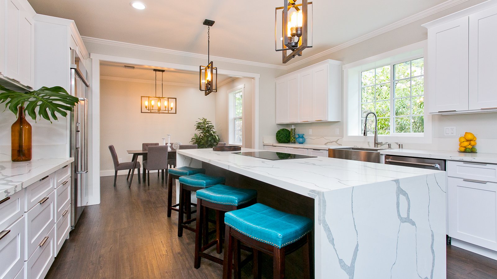 White kitchen with a waterfall quartz island and teal bar stools opening to a dining area