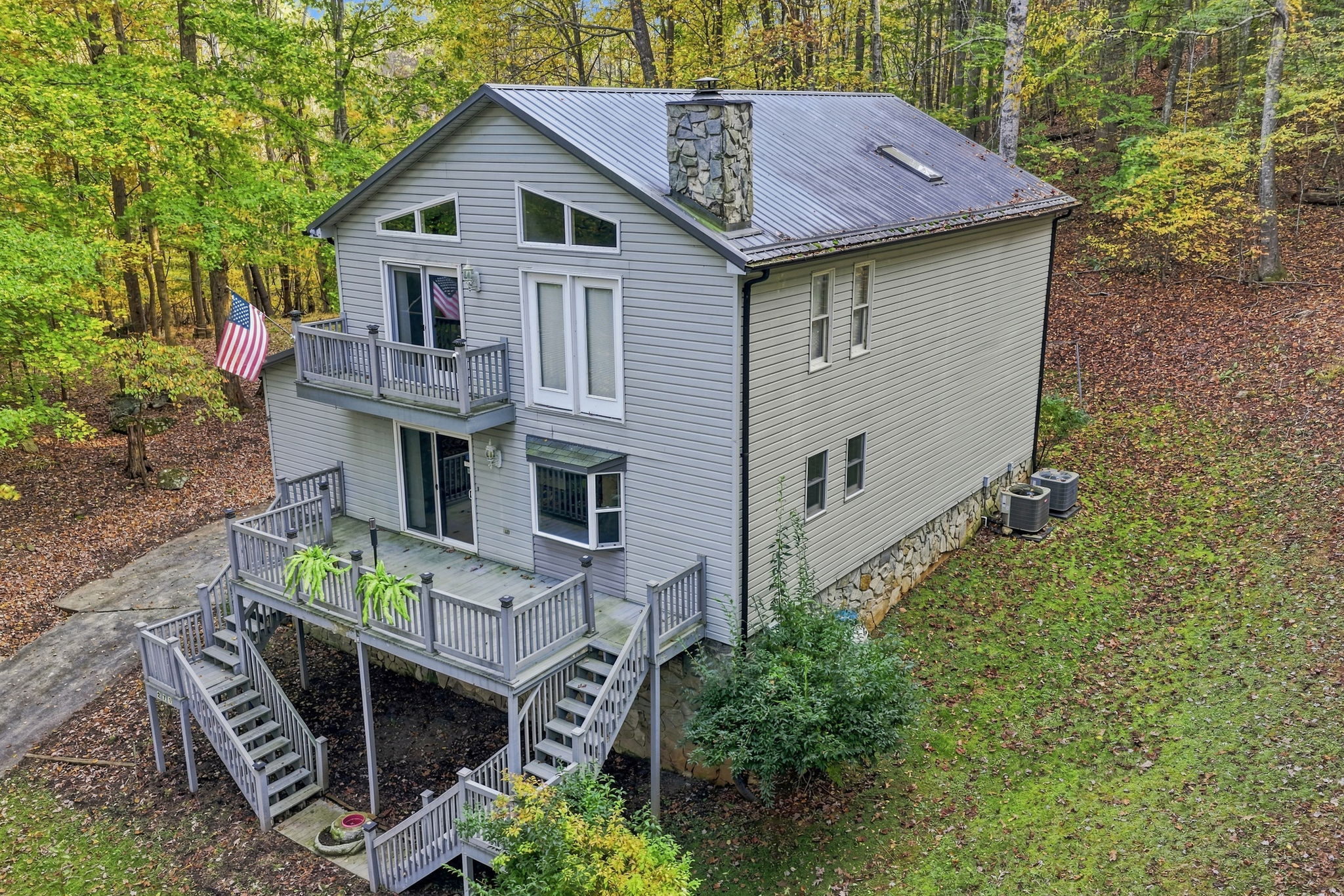 Actual elevated exterior photograph of the home showing the decks, roof, natural surroundings and exterior stairways