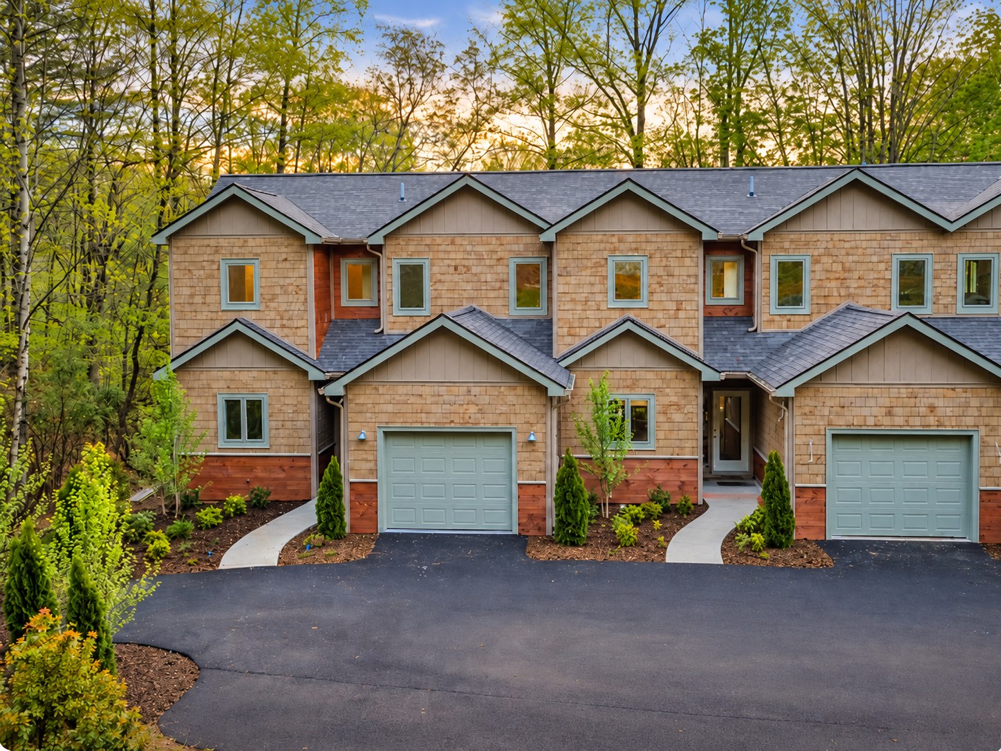 A row of connected mountain townhomes with individual garages and shared rooflines in a wooded setting