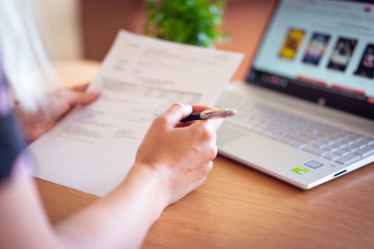 A person holding a paper and a pen next to a laptop