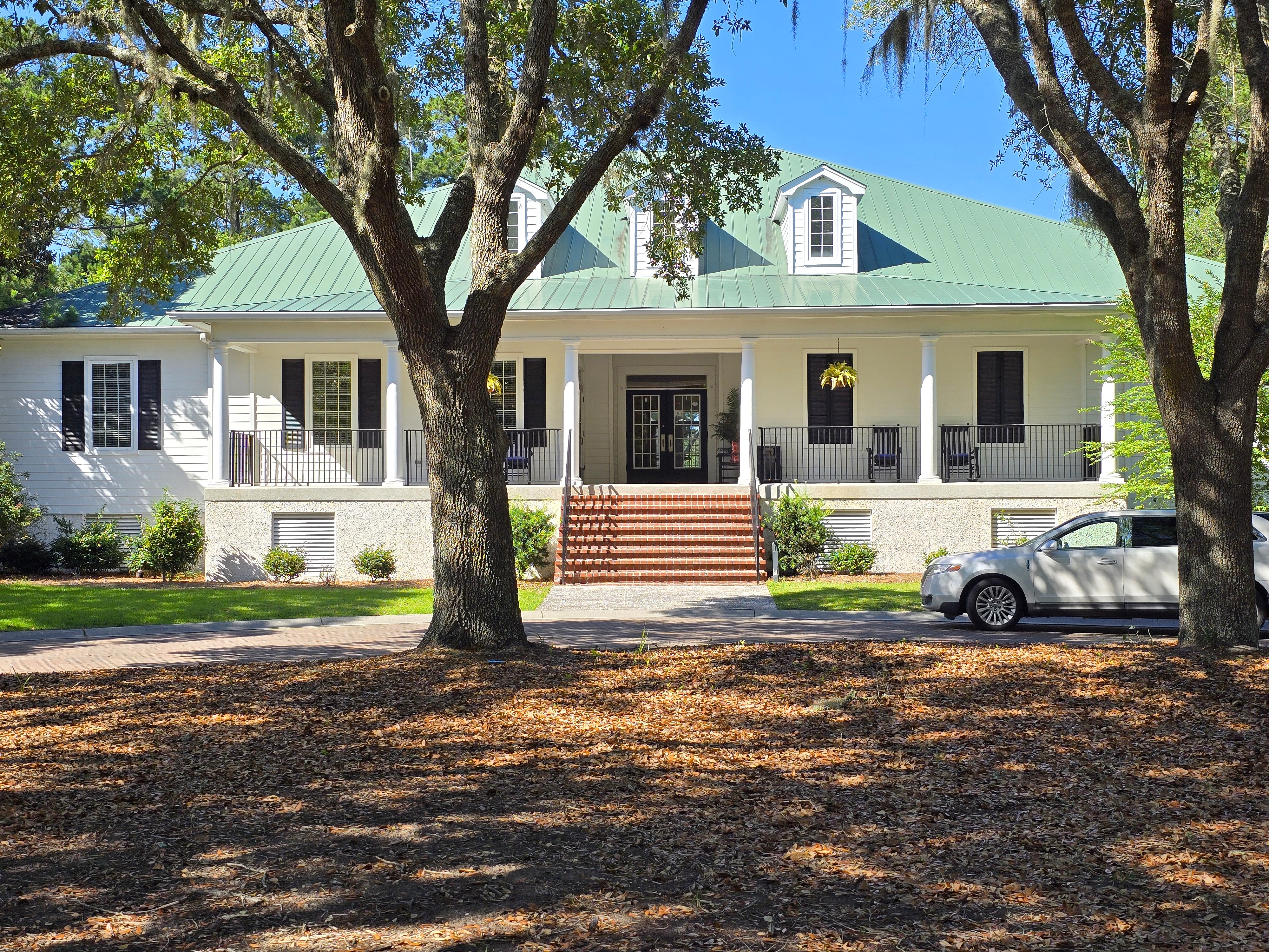 The Crescent Clubhouse in Bluffton SC -- classic Lowcountry architecture with raised foundation, wide front porch, and standing seam metal roof framed by live oaks