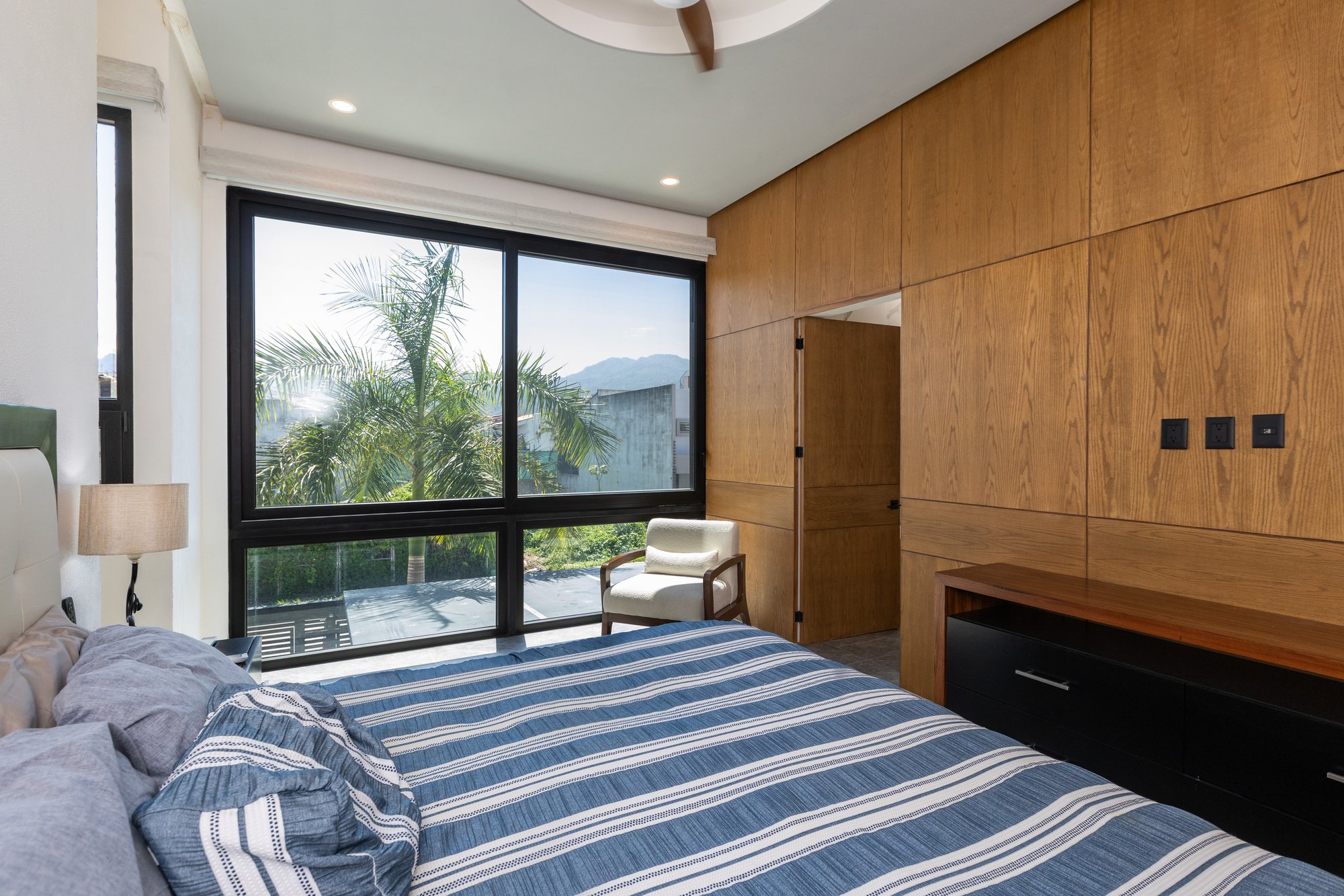 Primary bedroom with wood-paneled walls and a large window onto palms and mountains