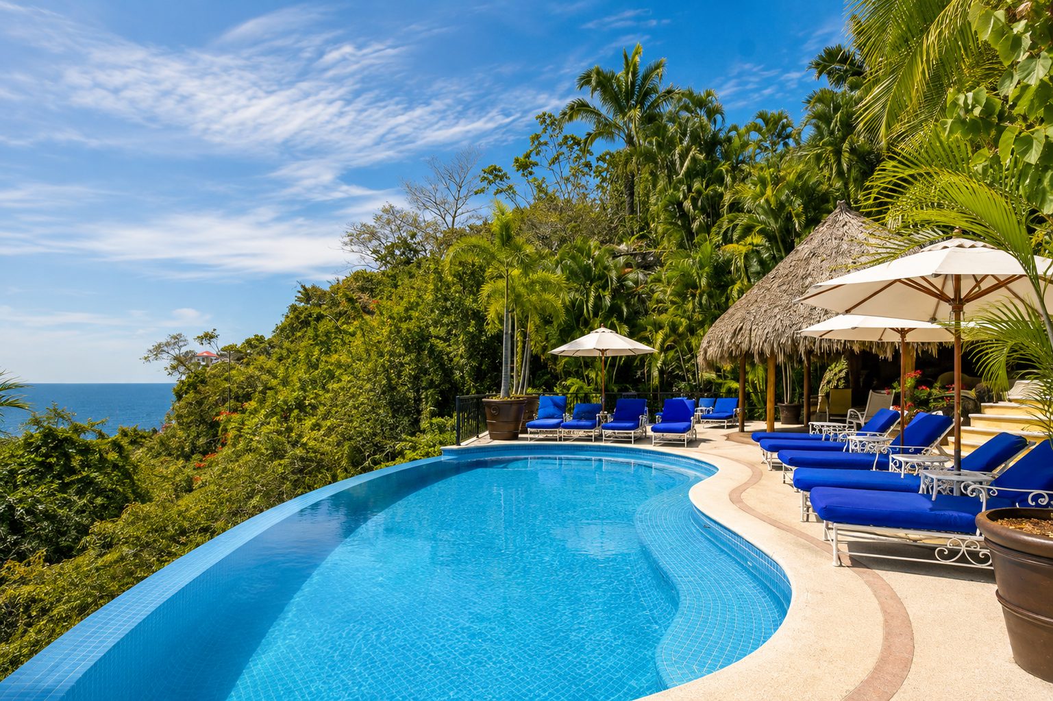 Pool with lounge chairs, umbrellas and palapa surrounded by jungle and ocean view