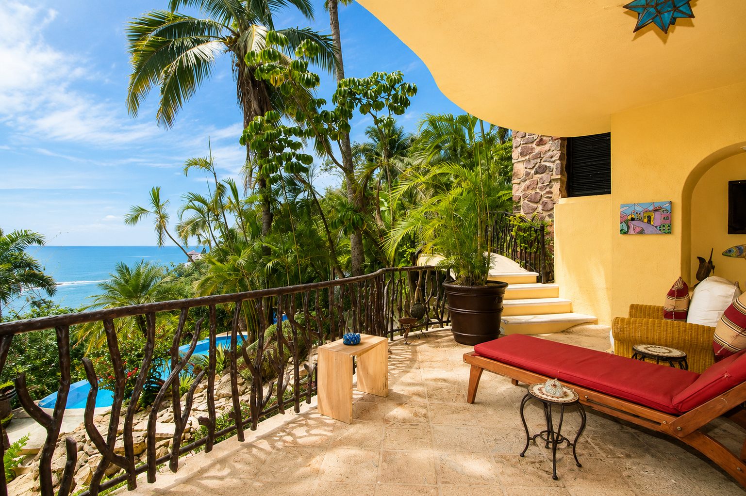 Shaded terrace with daybed and ironwork railing overlooking the pool and ocean