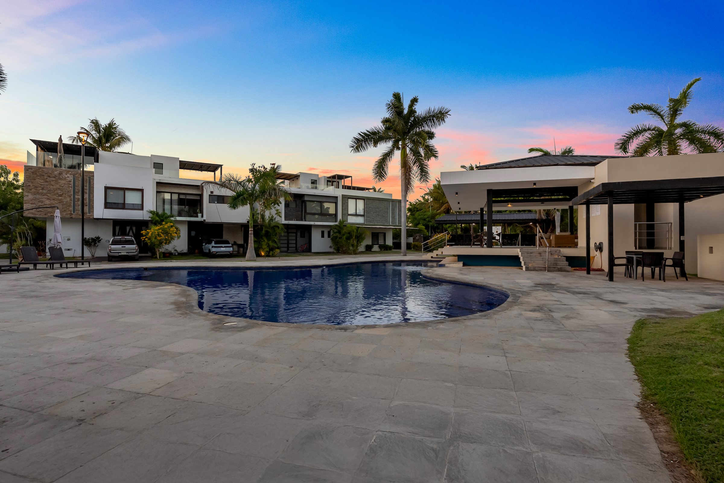 Alberca y casa club de la privada al atardecer, con las casas de la comunidad al fondo