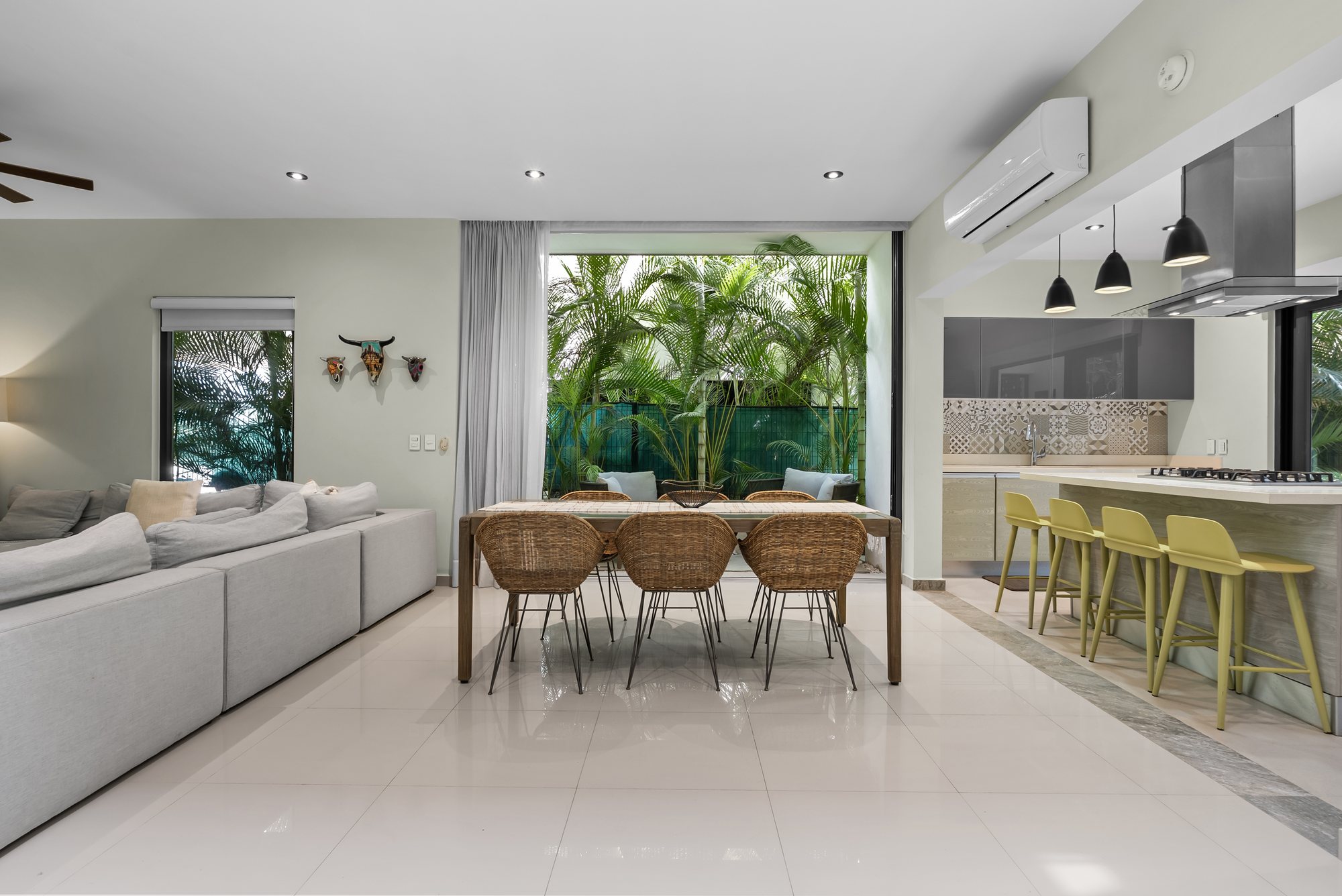 Sala, comedor y cocina abiertos con ventanales hacia las palmeras