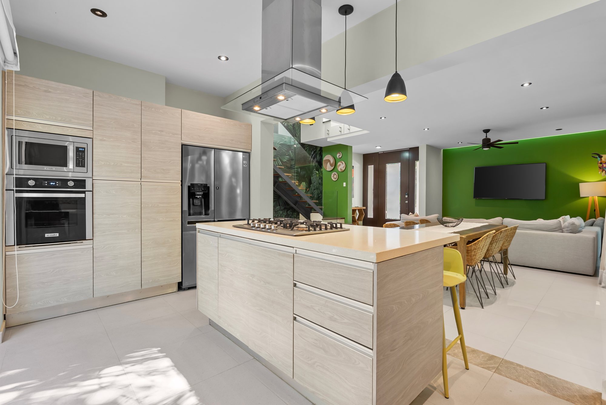 Isla de cocina con parrilla y campana de acero inoxidable, con la sala al fondo