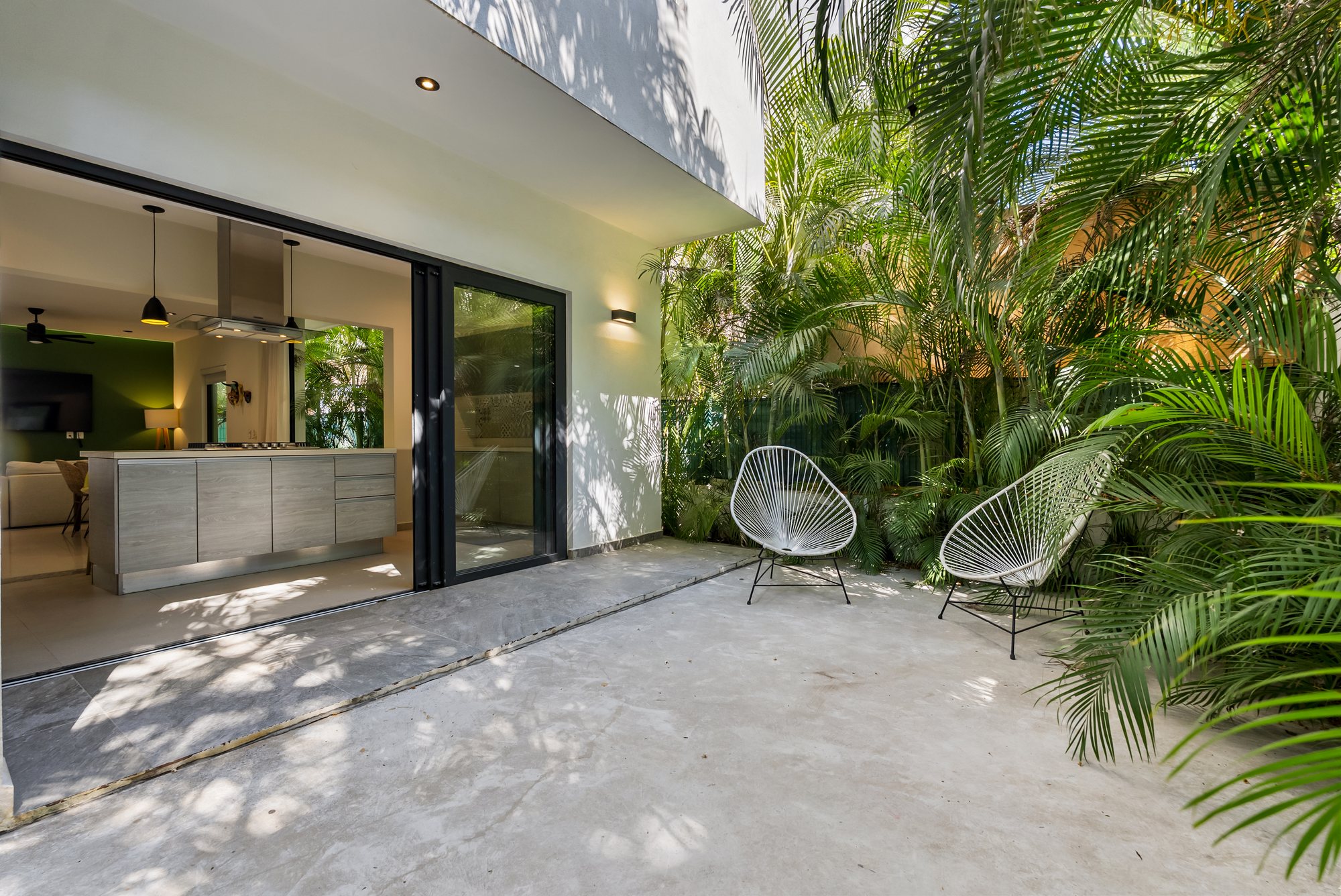 Patio trasero con sillas y palmeras, con la cocina tras las puertas corredizas de cristal