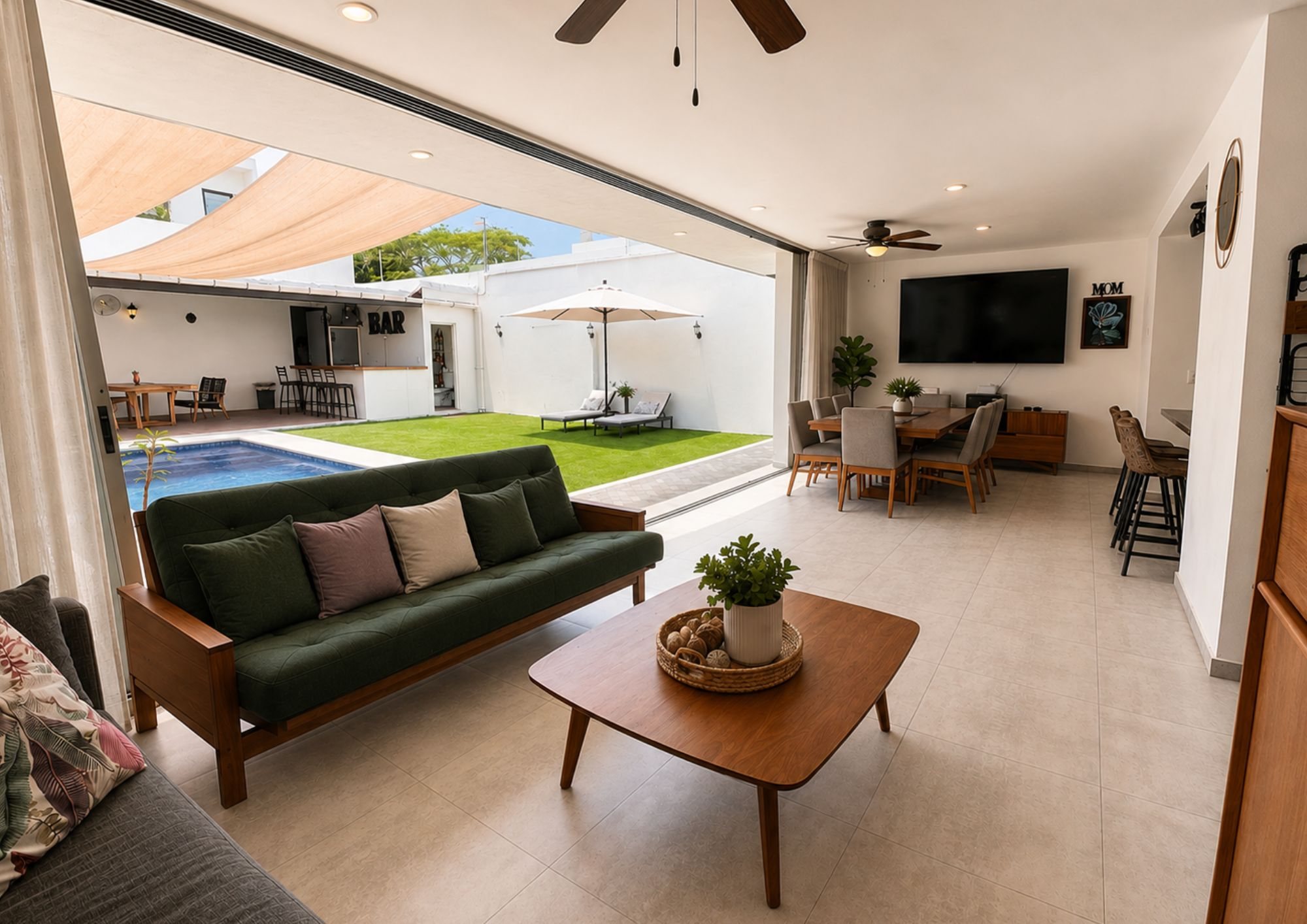 Sala con TV en la pared, abierta hacia el jardín y la alberca
