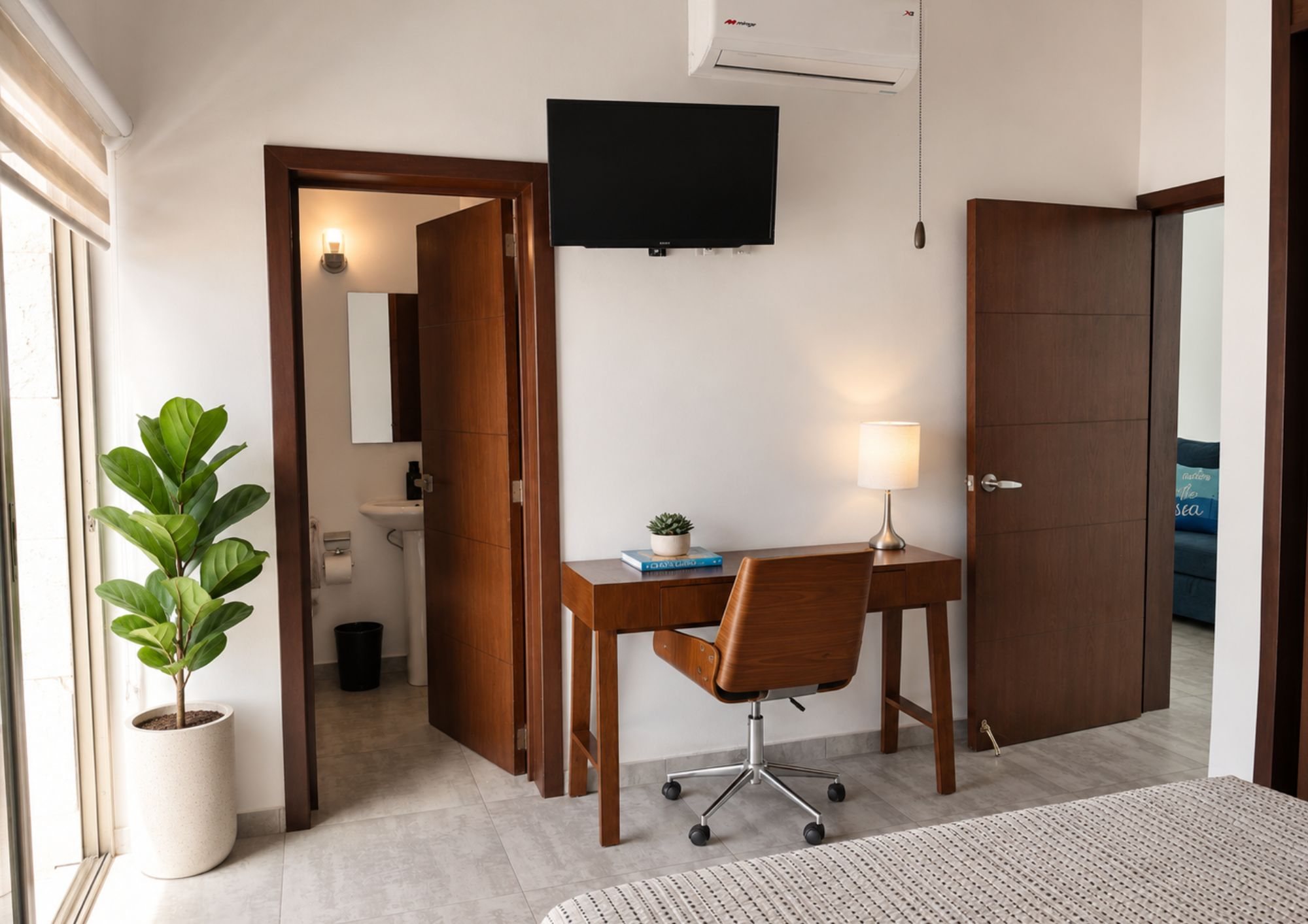 Rincón de recámara con escritorio, TV y puerta al baño