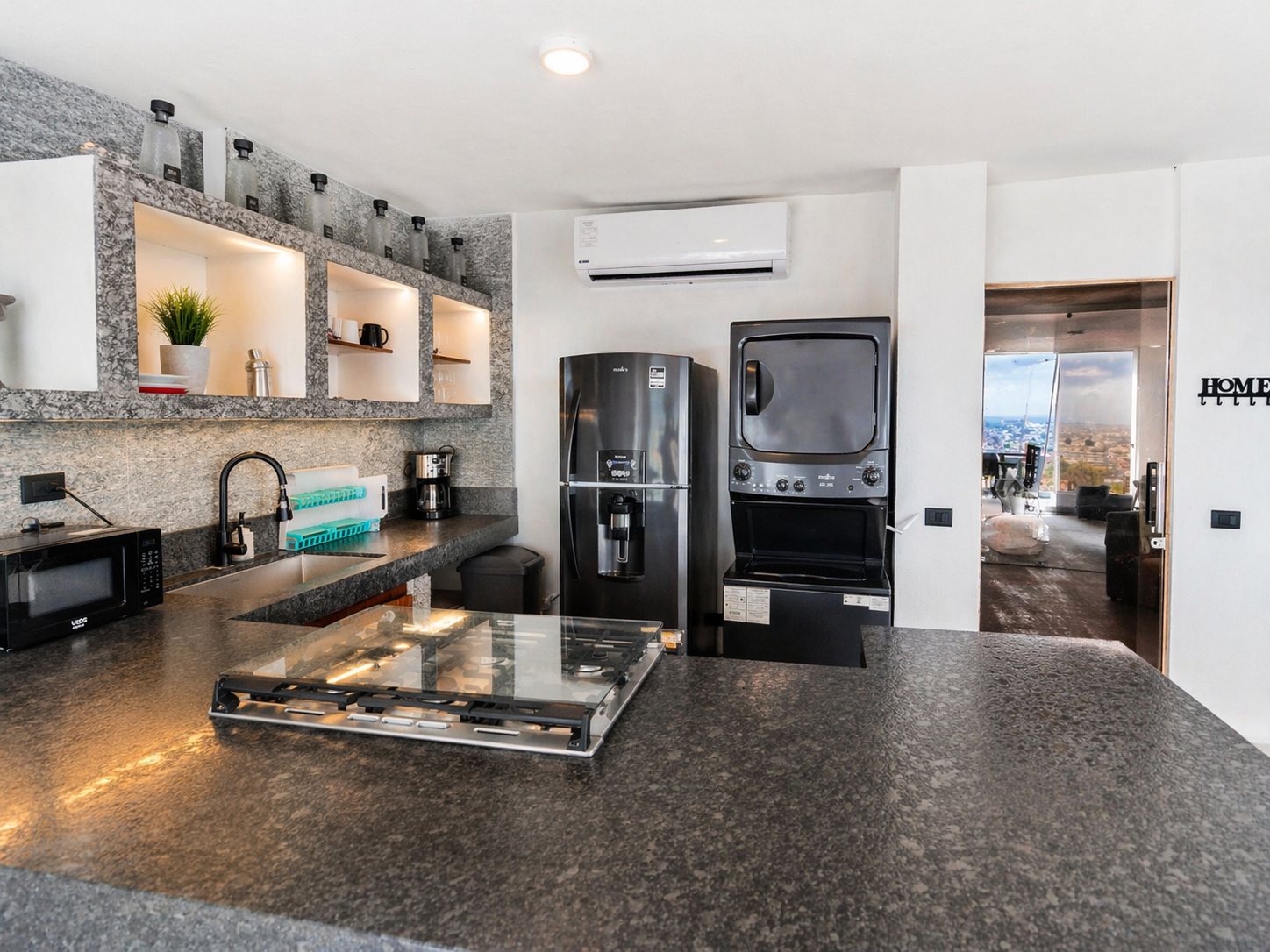 Cocina con cubierta de granito negro, repisas abiertas y lavadora y secadora apiladas