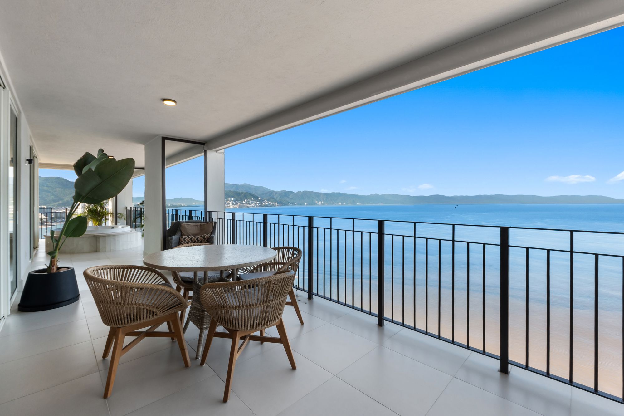 Covered terrace with a dining table and the bay and mountains beyond the railing