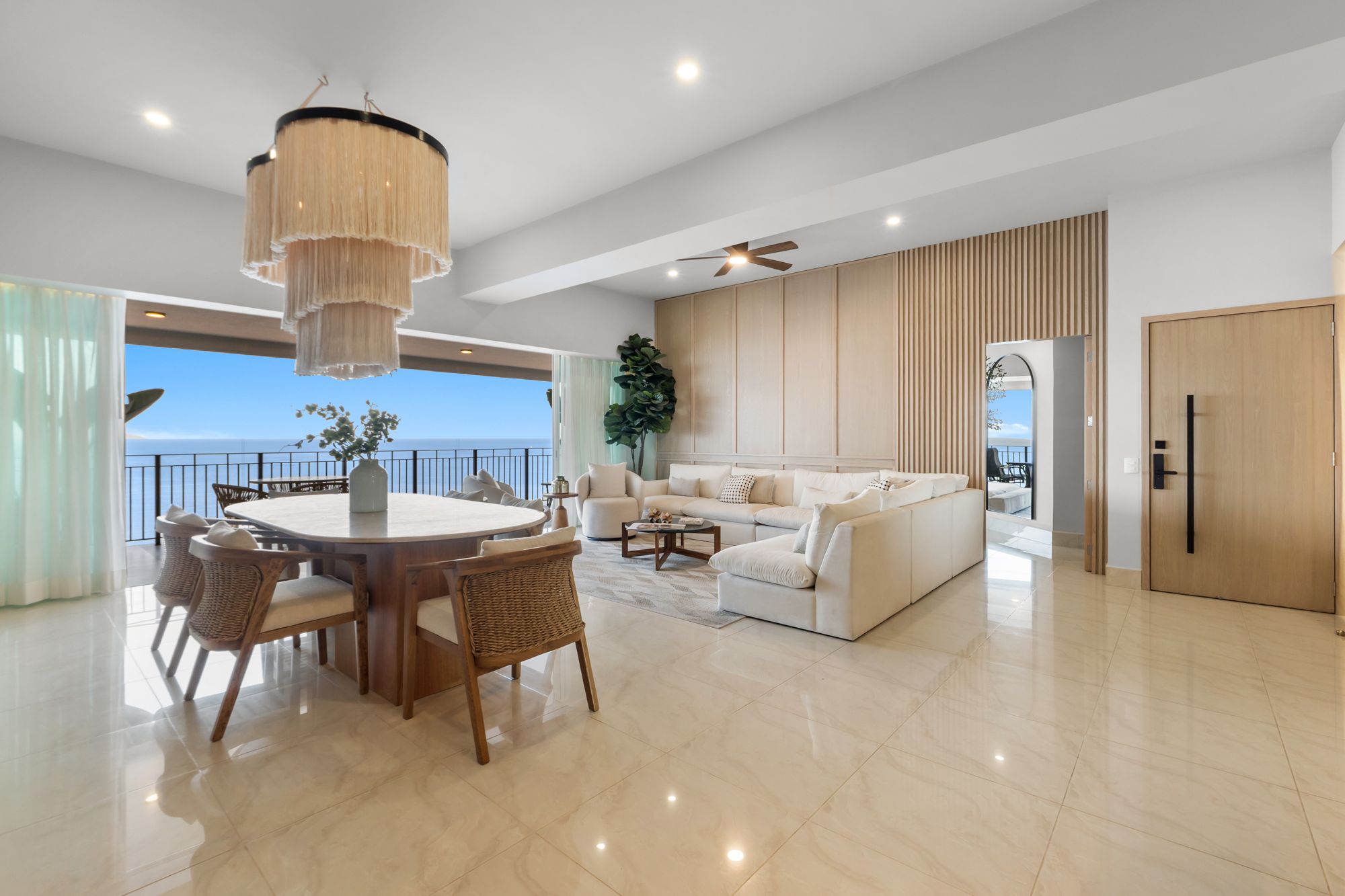 Dining table under a fringe chandelier with the ocean beyond
