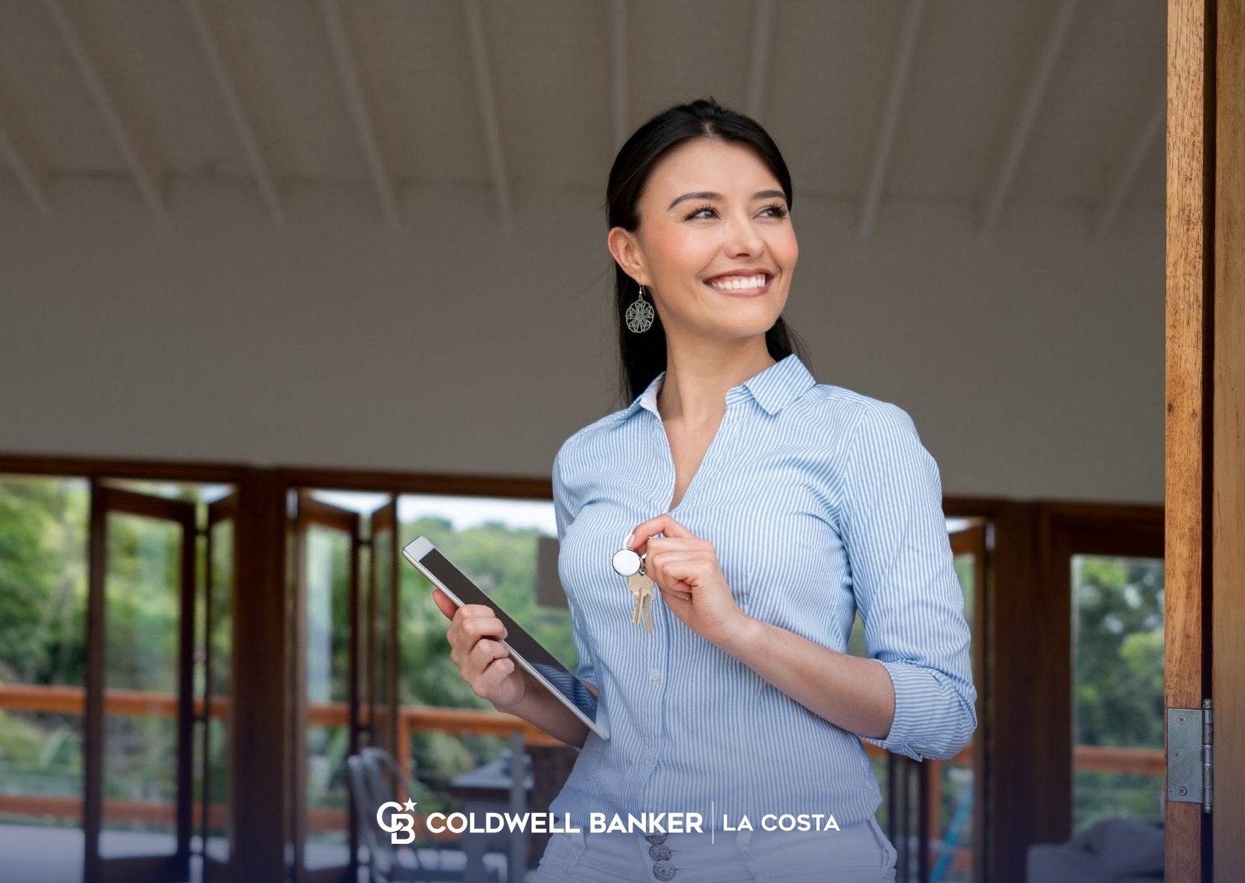 Smiling property manager holding keys and a tablet at the open door of a vacation rental in Puerto Vallarta