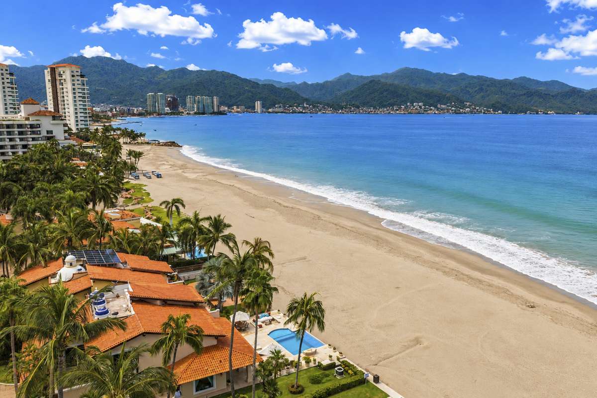 Vista aérea de las villas de Condominios Caracoles sobre la arena en Marina Vallarta, con la Bahía de Banderas al fondo