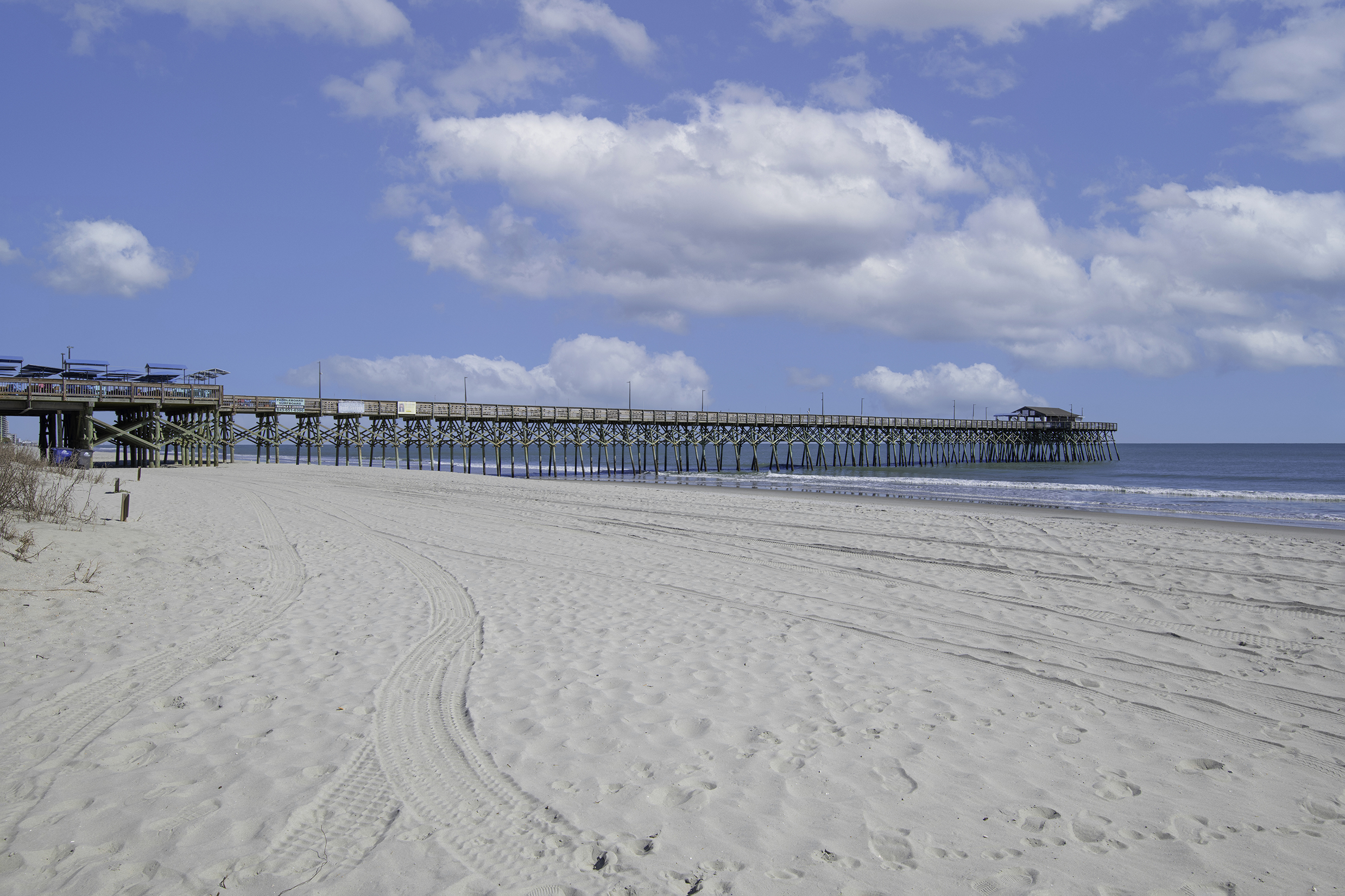A sunny day on the Garden City Beach by the pier where families enjoy fishing, swimming, fun at the arcade and the sound of live music while looking out over the blue waters of the Atlantic ocean.