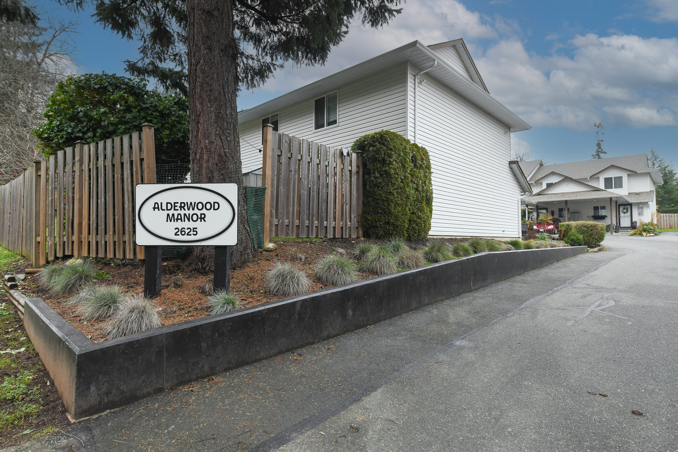 Exterior view of 15-2625 Muir Rd in Courtenay, BC, showcasing a well-maintained townhome complex with landscaped grounds, attached carport, and private patio spaces&mdash;highlighting desirable Courtenay East living close to schools, parks, North Island College, and everyday amenities on Vancouver Island.