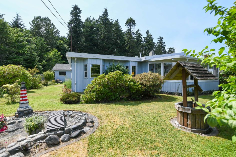 Highlights the West Coast rancher at 5340 Gainsberg Rd in Deep Bay, featuring vaulted ceilings, a jetted soaker tub, sunroom, detached shop, and backyard with covered deck overlooking forested trails, now listed at $799,000.