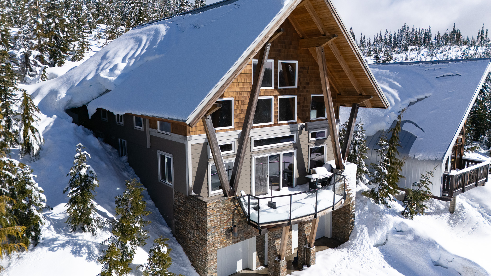 Exterior view of 570 Arrowsmith Ridge in Beaufort Heights near Mount Washington, showcasing a modern alpine chalet with dramatic mountain architecture, large cathedral windows, and breathtaking views toward Strathcona Park, highlighting its four-season mountain retreat setting and proximity to the Nordic Lodge and Alpine Resort.