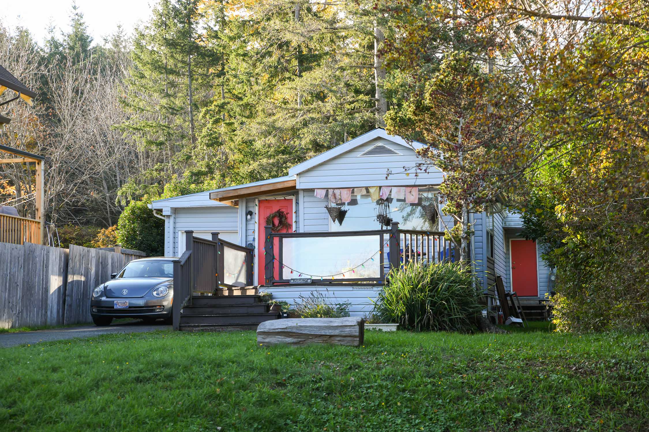 Front exterior view of a charming 3-bedroom manufactured home in Union Bay. The home features a spacious front patio with peek-a-boo ocean views, surrounded by a neatly kept yard. A single garage sits to one side, and the exterior is bright and welcoming, reflecting the relaxed coastal lifestyle of this seaside community.