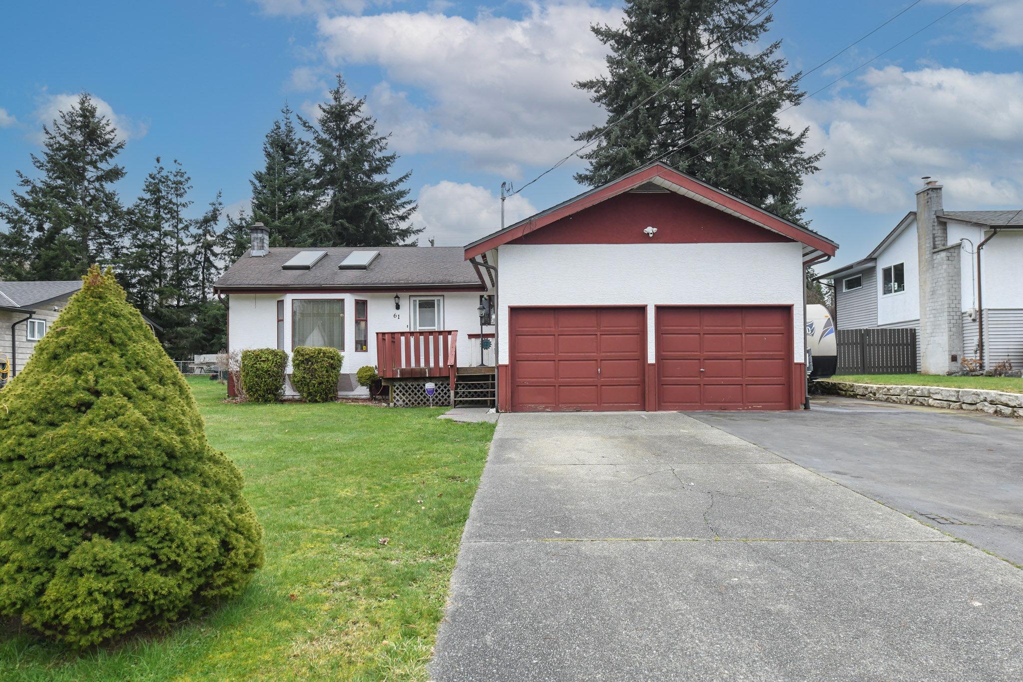 Front exterior of a single-level rancher set on a spacious 0.34-acre lot in a quiet West Courtenay neighborhood. The home features a welcoming driveway with ample parking, including space for RV parking, and an attached double garage. Mature landscaping surrounds the property, creating a peaceful residential setting while still being close to amenities and outdoor recreation near the Puntledge River.