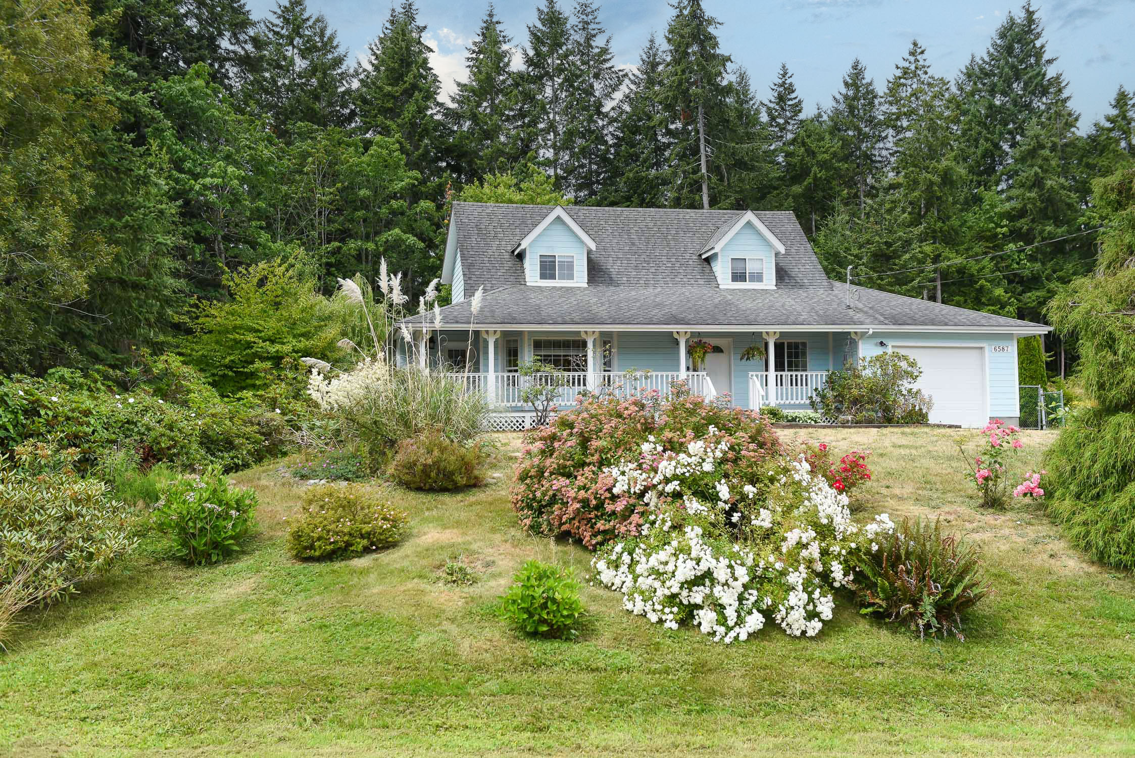Charming farmhouse-style home at 6587 Mystery Beach Rd near Fanny Bay featuring mature trees, established gardens, a covered patio, peaceful stream with arched bridge, goldfish pond, and exceptional privacy in a beautiful country setting.