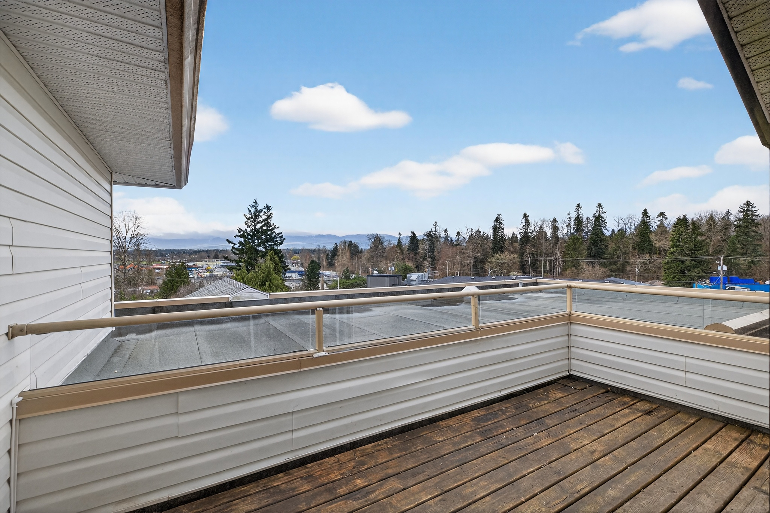 View from a top-floor, south-facing balcony overlooking sweeping mountain vistas and a bright, open skyline. The elevated perspective captures abundant natural light throughout the day, with surrounding rooftops and treetops leading toward the distant mountains. This private outdoor space offers a peaceful setting to relax and take in the scenic beauty of Courtenay.