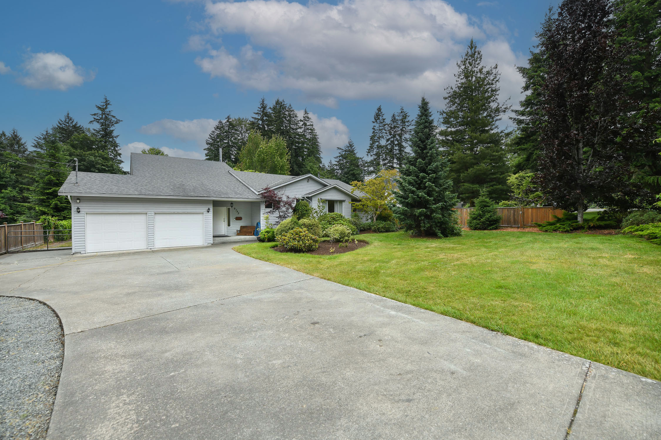 Exterior view of 8732 Paulsen Rd in Black Creek, BC&mdash;showcasing a spacious family home set on a private 1.07-acre lot. The front of the house features well-maintained landscaping, mature trees, a large driveway with ample parking, and a peaceful rural setting. This Vancouver Island acreage property highlights the home&rsquo;s inviting curb appeal, natural surroundings, and quiet location near Miracle Beach and Saratoga Beach.