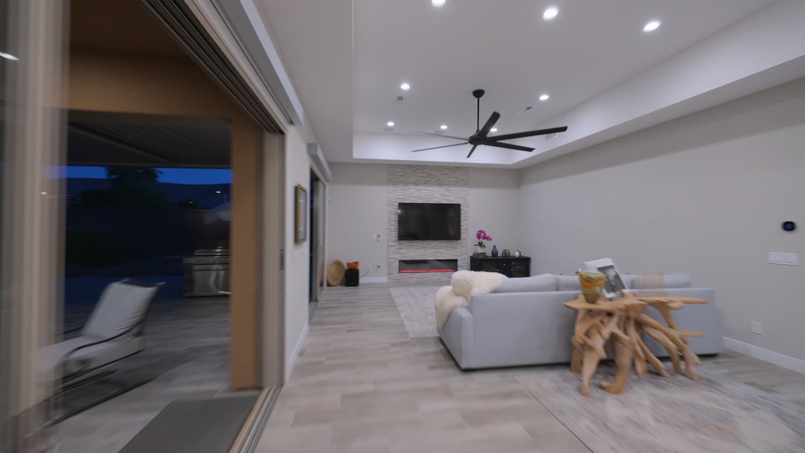 Open-concept living room with tray ceiling, linear fireplace and sliding glass walls to a covered patio