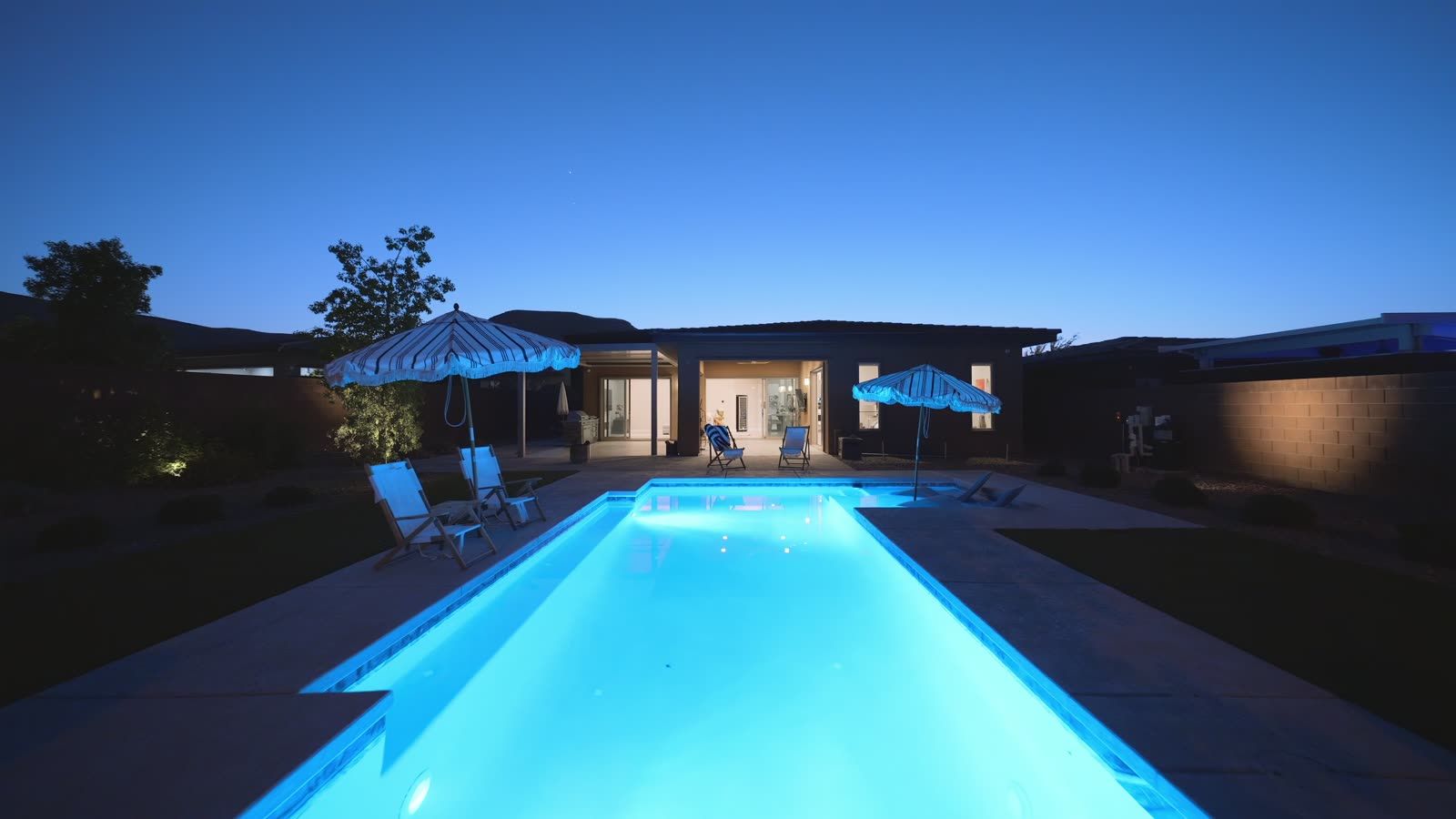 Lit swimming pool and covered patio of a modern single-story home at twilight