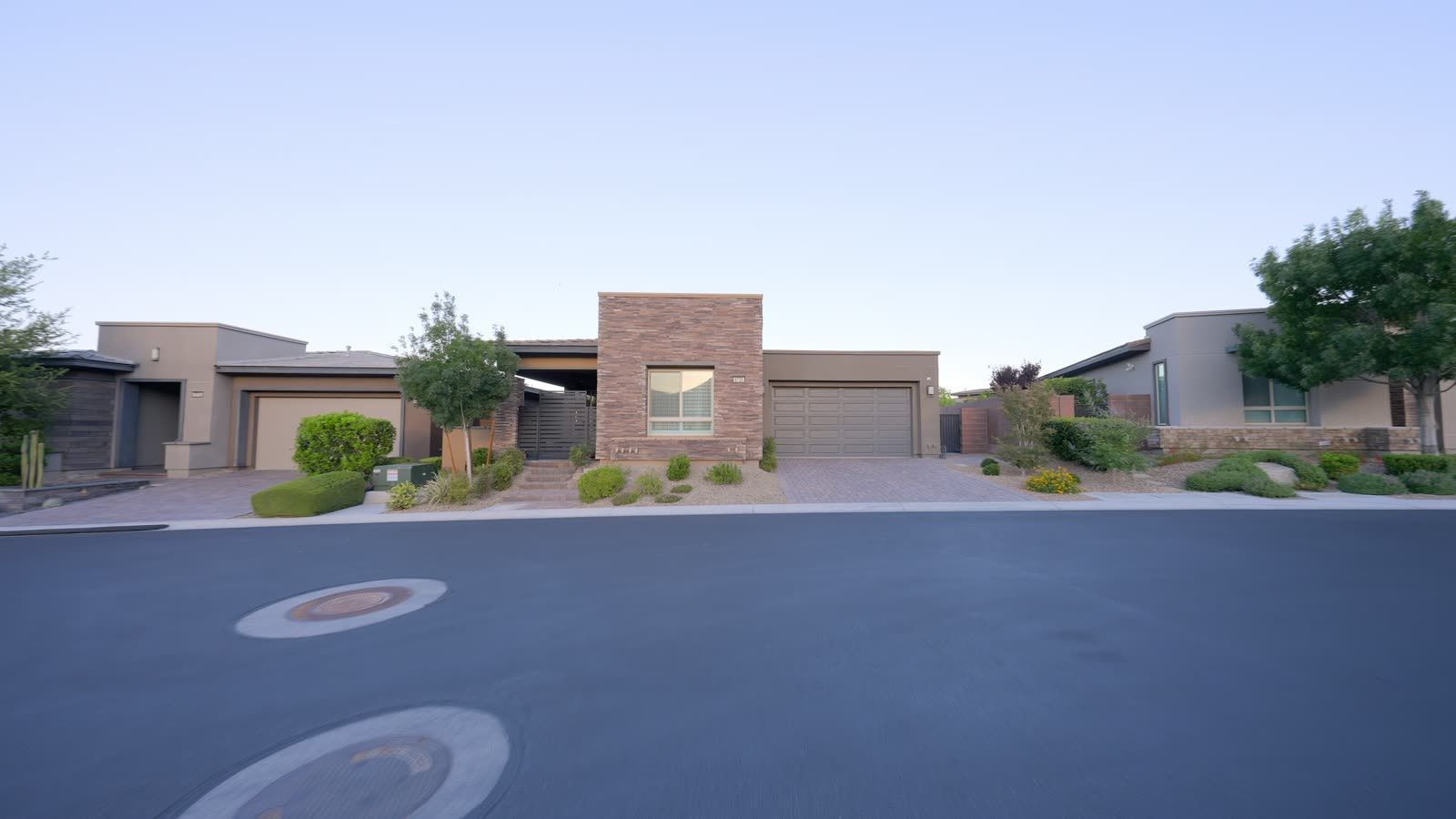 Modern single-story homes along a quiet residential street at dusk