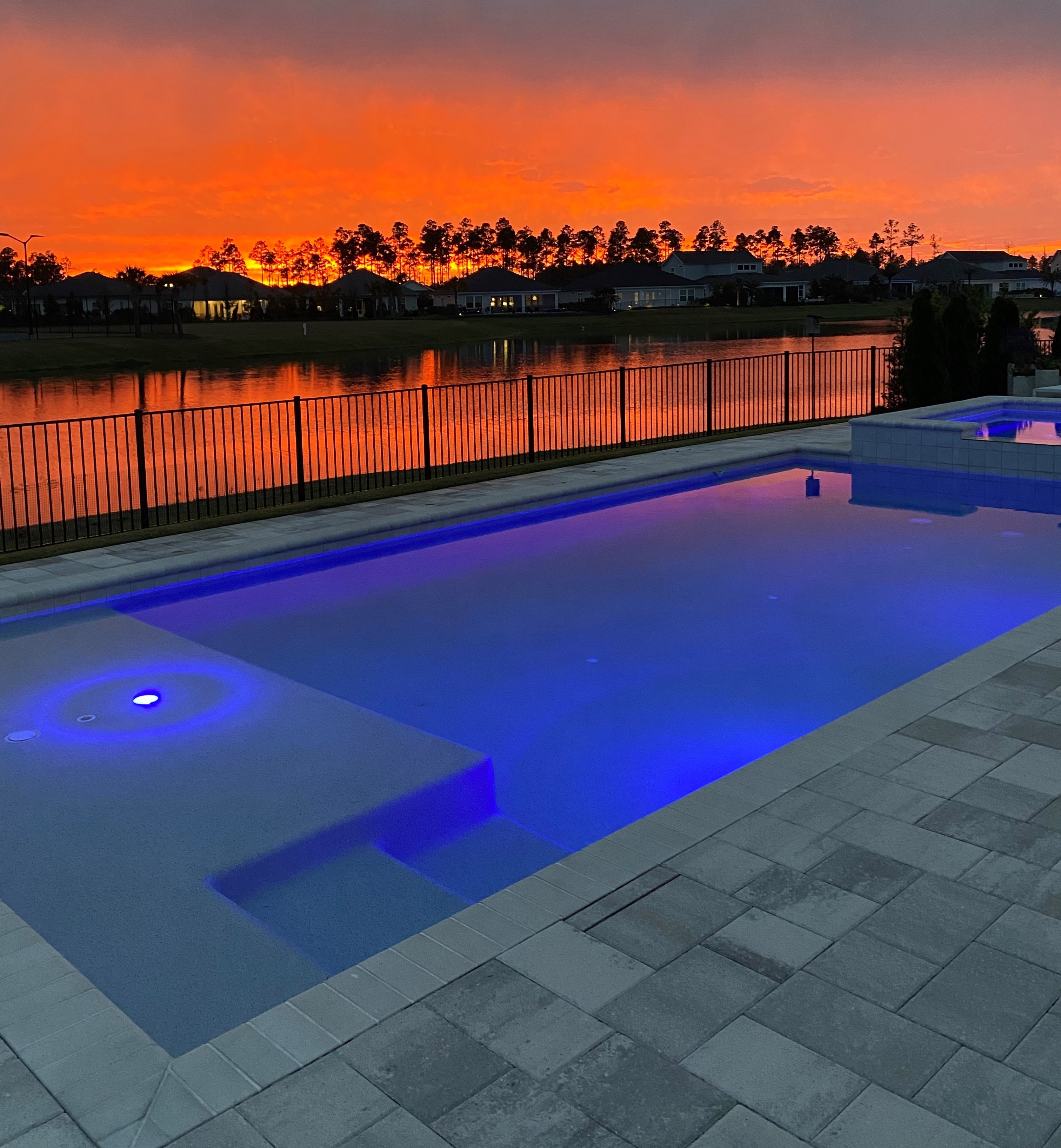 Sunset over the pond behind a home in NatureWalk at Watersound Origins, with a lit blue pool in the foreground