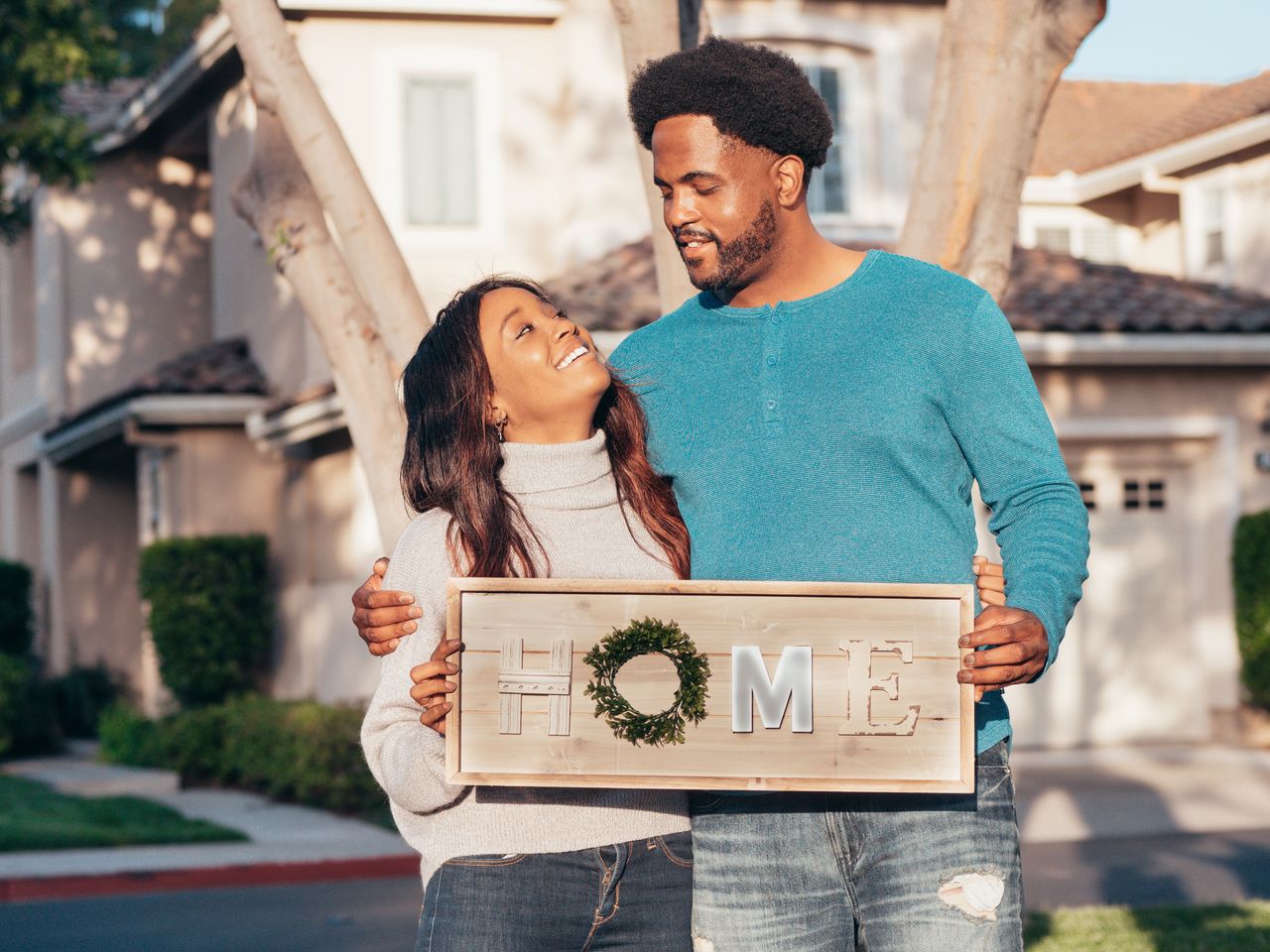 young couple holding home sign in front of house