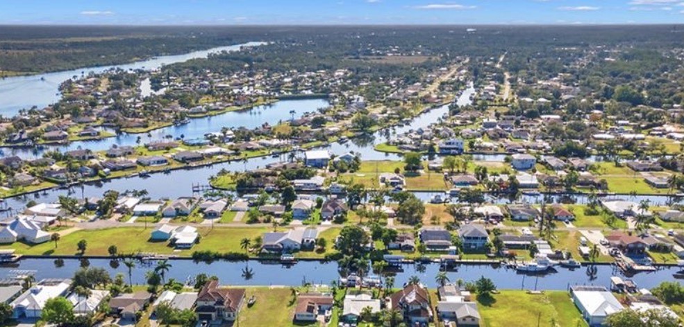 An aerial view of Fort Myers Shores showcases tree-lined streets and beautiful waterfront homes along the Caloosahatchee River, highlighting the area's appeal for prospective property consumers interested in real estate listings in Fort Myers, FL. The image captures the serene landscape and residential charm, making it a perfect spot for buyers looking for homes for sale.